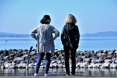 two woman standing in front of ocean rocks during daytime thumbnail