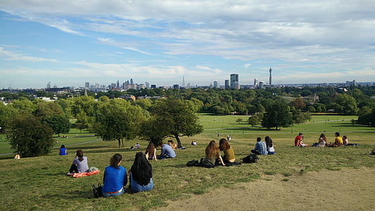 group of people sitting on grass field with trees and buildings as background thumbnail