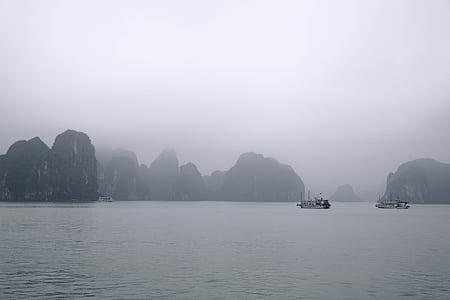 two white boat near islands covered with fog at daytime thumbnail
