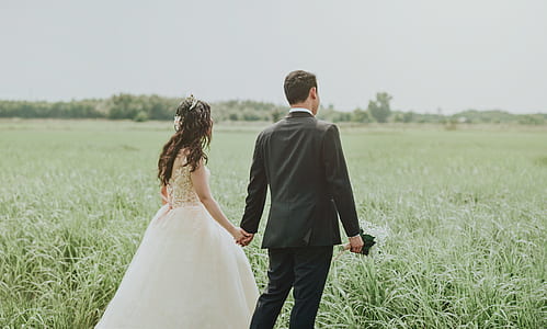 Woman in White Wedding Dress Holding Hand to Man in Black Suit thumbnail