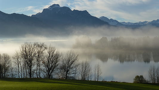 body of water covered with fog near mountain range thumbnail