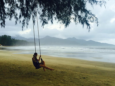 woman sitting on swing attached on tree on seashore thumbnail