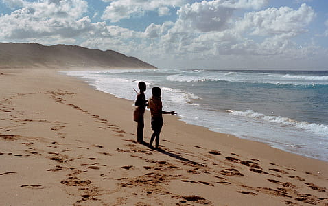 Two Children Stands on Shore Near Ocean at Daytime thumbnail