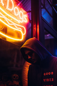 man wearing hoodie standing near neon signage thumbnail