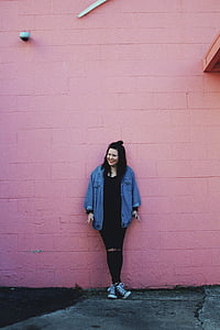 smiling woman leaning on pink concrete wall during daytime thumbnail