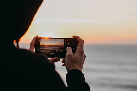 person holding black smartphone while taking picture of body of water during daytime thumbnail