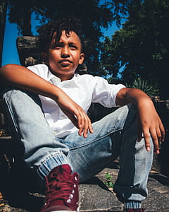 Boy in White Shirt and Faded Blue Jeans Sitting on Ground thumbnail