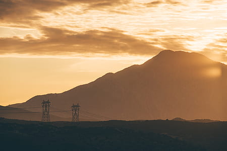 silhouette of mountain and utilitypoles during orange sunset thumbnail