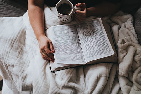 person holding mug and book laying on gray surface thumbnail