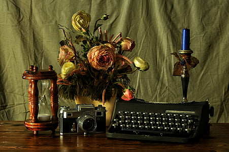 typewriter beside camera, hourglass, flower decor, and candlestick with candle on table thumbnail