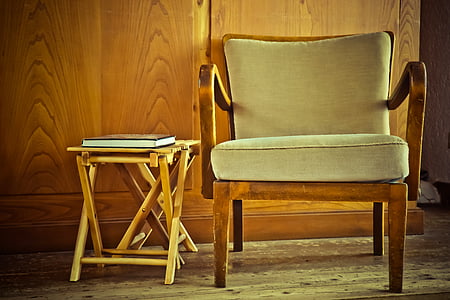 book on brown wooden side table beside wooden armchair thumbnail