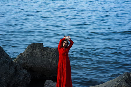 man in red sari dress standing on boulders near body of water thumbnail