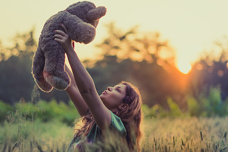 woman in green shirt holding brown teddy bear during sunrise thumbnail