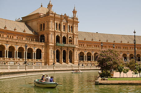 people boating on canal near red concrete building during daytime thumbnail