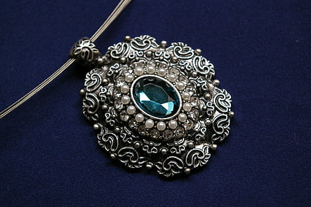 silver-colored pendant with cyan gemstone on blue velvet textile thumbnail