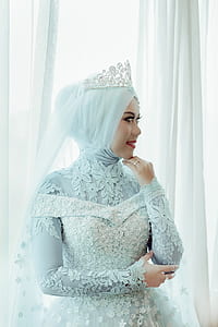 woman standing near window while wearing blue floral hijab wedding dress thumbnail