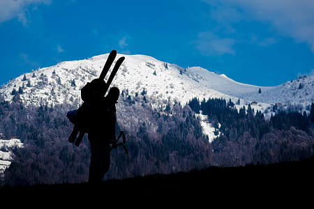 silhouette of man carrying backpack and snow ski blades with distance at snow capped mountains thumbnail