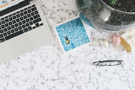 flat lay photography of MacBook beside pineapple card and black framed eyeglasses on black and white marble surface thumbnail
