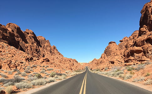 two yellow line asphalt road between brown rock cliffs during daytime thumbnail