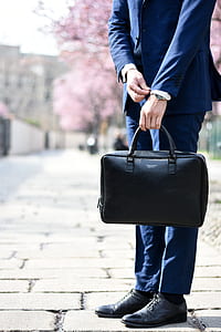 man in blue suit jacket with dress pants and pair of black leather dress shoes outfit holding black handbag during daytime thumbnail