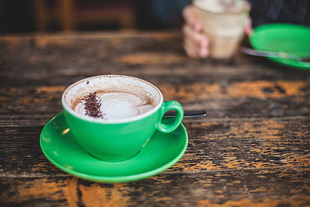 brown coffee filled green ceramic cup with saucer on top of brown table thumbnail
