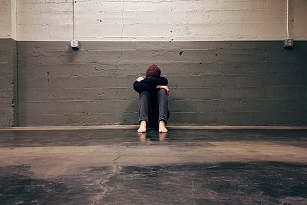person sitting on floor leaning on gray concrete wall thumbnail