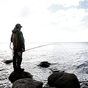 man standing on rock holding fishing rod thumbnail