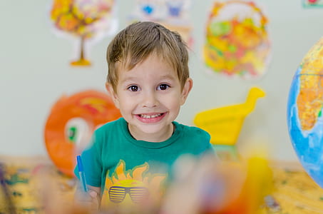 selective focus photo of a boy holding a blue pen smiling while taking a photo thumbnail