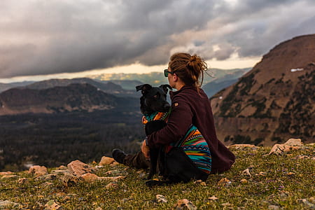 woman sits on grass hugging her black dog during daytime thumbnail