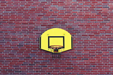 yellow-and-black basketball board and hoop on red-and-black brick wall during daytime thumbnail
