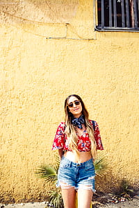 woman in red crop top and blue denim distressed shorts in front of yellow paint wall thumbnail