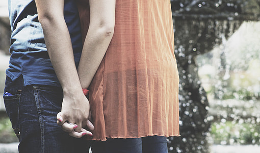 man wearing blue-washed denim bottoms holding hands with woman wearing peach-colored top thumbnail