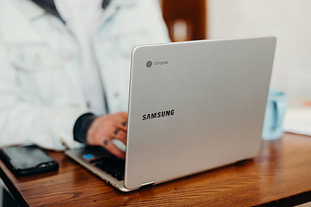 person using gray and black Samsung Chromebook on brown wooden desk thumbnail