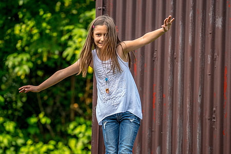 brown haired girl in white tank top standing behind brown galvanized iron sheet thumbnail