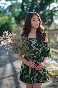 woman wearing green and white bird print off-shoulder dress while holding purple flowers thumbnail