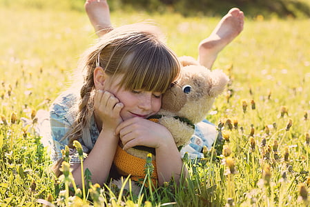 girl with brown bear push toy smiling white lying on grass field thumbnail