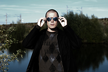 man wearing jacket holding his sunglasses near body of water thumbnail
