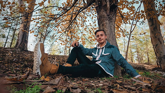Man Wearing Green Jacket Sitting on Ground Near Tree thumbnail