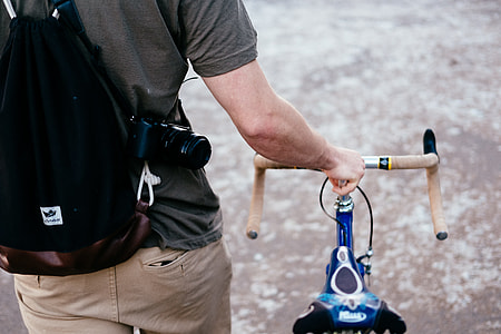 person wearing gray shirt with black backpack near blue bike thumbnail