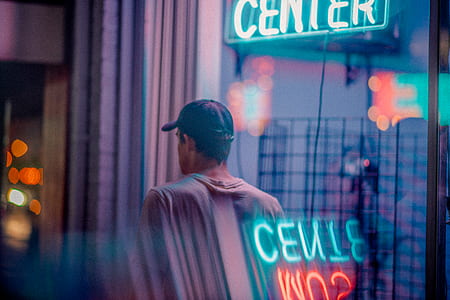 man in gray shirt standing near center neon signage thumbnail