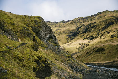 A young Caucasian hiker green hills near glacial stream thumbnail