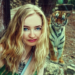 woman wearing blue shirt taking photo near the tiger during daytime thumbnail