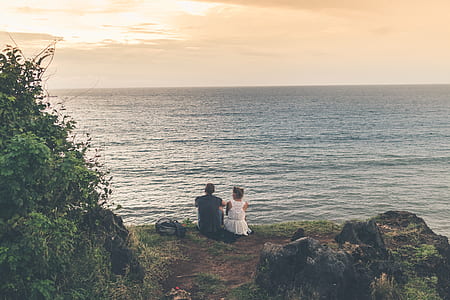man and woman sitting on cliff near wave of sea thumbnail