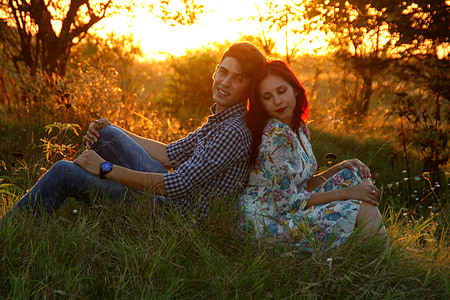 man and woman leaning to each other sitting on grass field during golden hour thumbnail