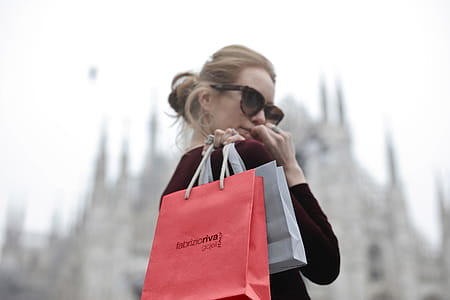 A young blonde woman wearing a red dress holding shopping bags in her hand looks over her shoulder thumbnail