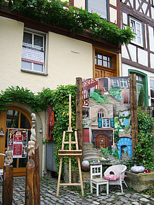 brown easel stand beside painting in front of building thumbnail