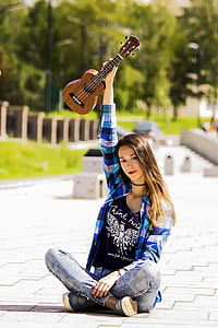 woman sitting on concrete pavement holding travel acoustic guitar thumbnail