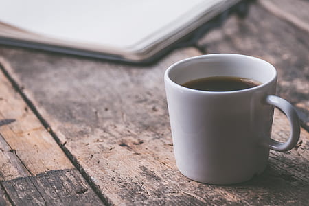 white mug beside book on brown board thumbnail