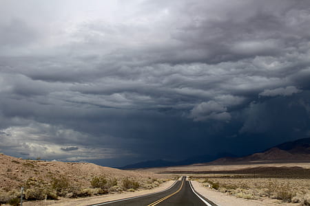 asphalt road between desert under dark cloudy sky thumbnail