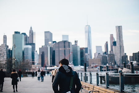 man walking near body of water and high-rise buildings at daytime thumbnail